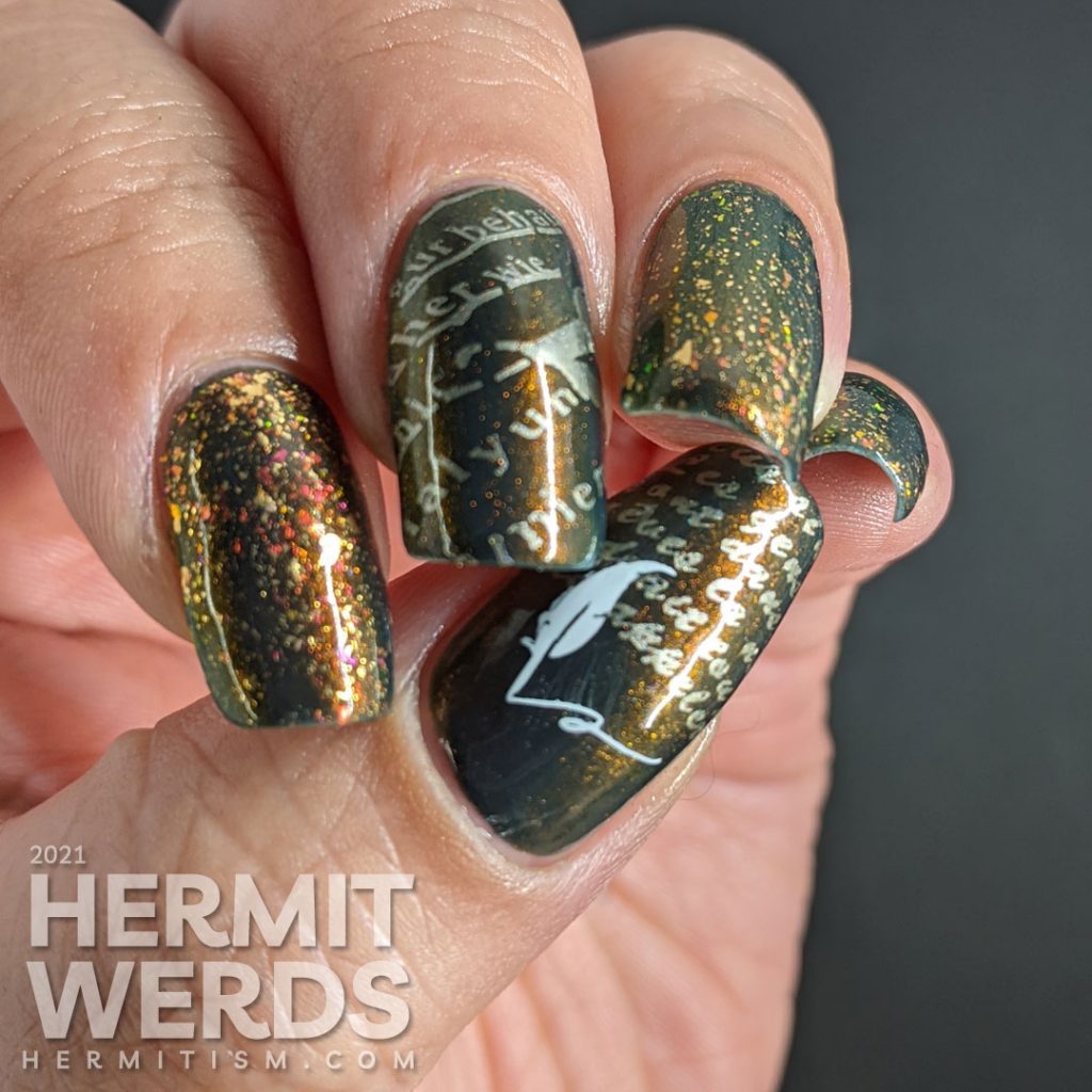 A smoky navy blue multichrome nail art with fake writing being highlighted (alphabet) stamping decals topped with a gold/iridescent topper.