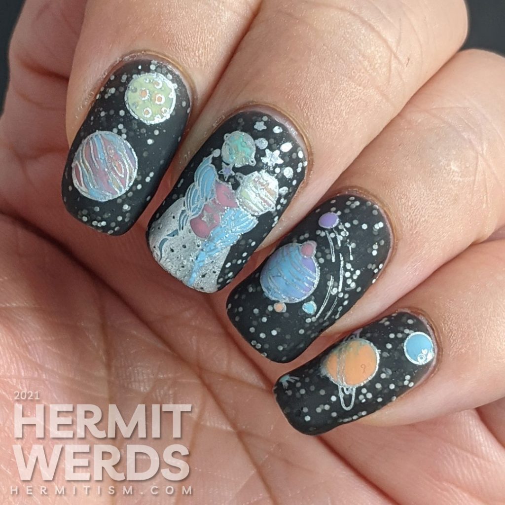 An outer space mani, with a field of stars created by white glitter in a black jelly and colorful stamping images of planets and a planet-headed lady.