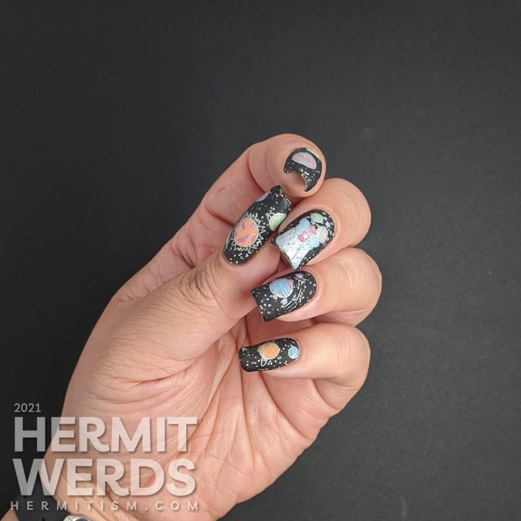 An outer space mani, with a field of stars created by white glitter in a black jelly and colorful stamping images of planets and a planet-headed lady.