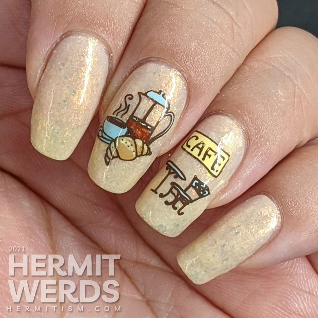 French nail art on a flakie-filled cream crelly  with stamping decals of delicious French food like wine, croissants, and french press coffee. 