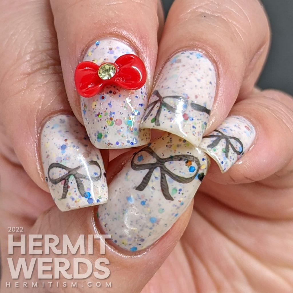 Nail art covered with bows including a bow nail charm on top of a white crelly filled with rainbow glitters.