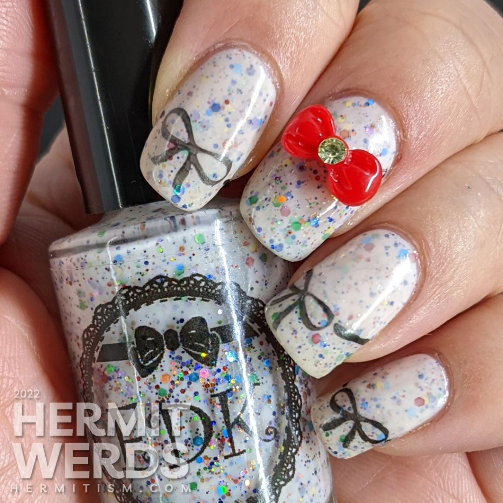 Nail art covered with bows including a bow nail charm on top of a white crelly filled with rainbow glitters.