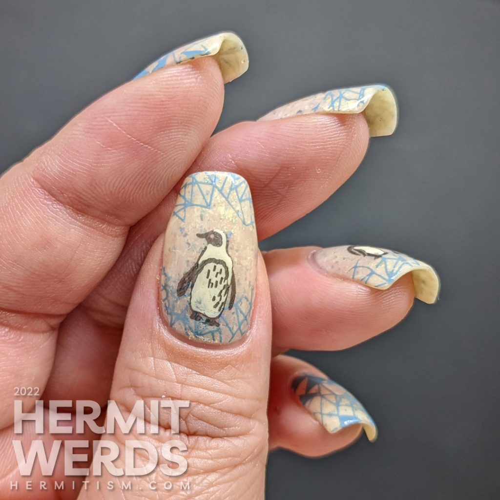 Soft penguin nail art with metallic black stamping images of fanciful penguins and grey-blue geometric ice patterns.