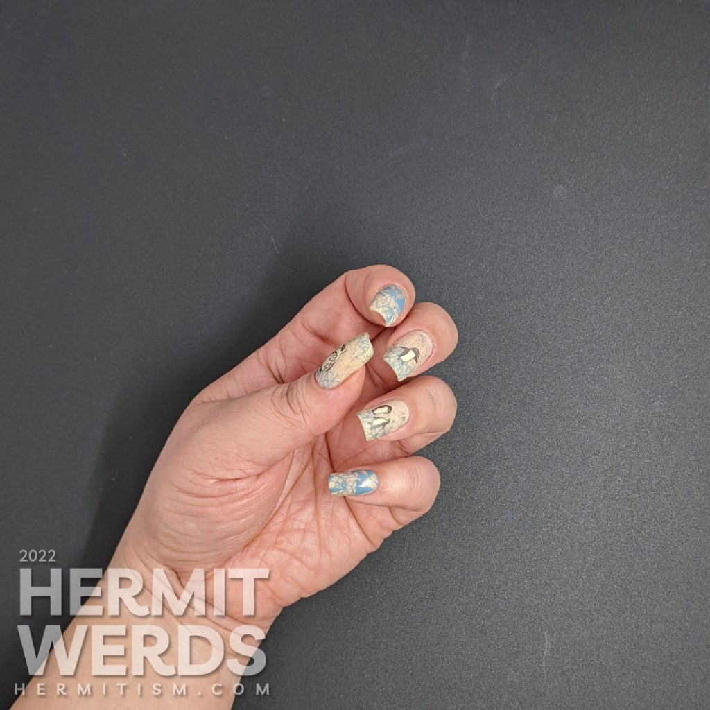 Soft penguin nail art with metallic black stamping images of fanciful penguins and grey-blue geometric ice patterns.