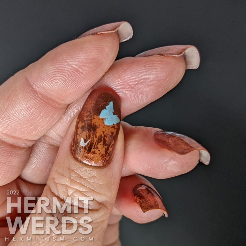 A coppery-y floral mani with a magnetic copper base and simple stamping images of a floral field and tiny baby blue and white butterflies.