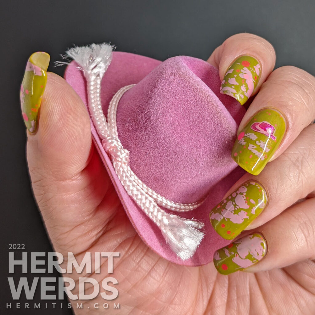 Cowgirl nail art on a green base with pink glitters, pink stamping decals of pink cowhide print, cowboy hat, and cowgirl with a "bang" flag.