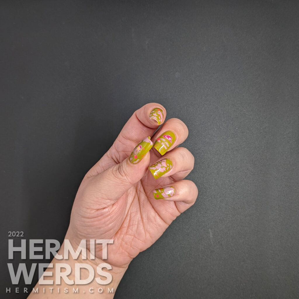 Cowgirl nail art on a green base with pink glitters, pink stamping decals of pink cowhide print, cowboy hat, and cowgirl with a "bang" flag.