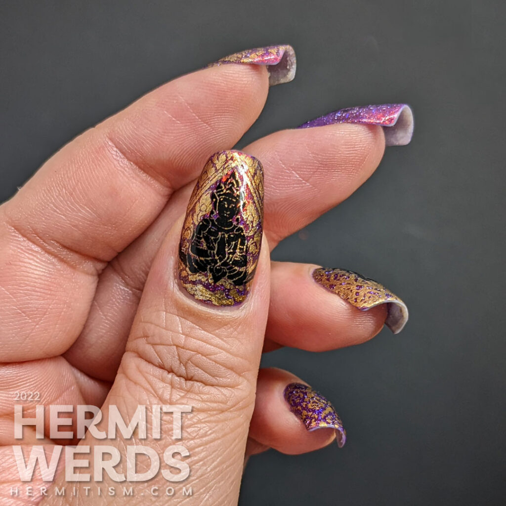 A brocade-like Thailand nail art featuring Buddah meditating over a lotus blossom + a Thai flame fabric pattern over a flakie purple polish.