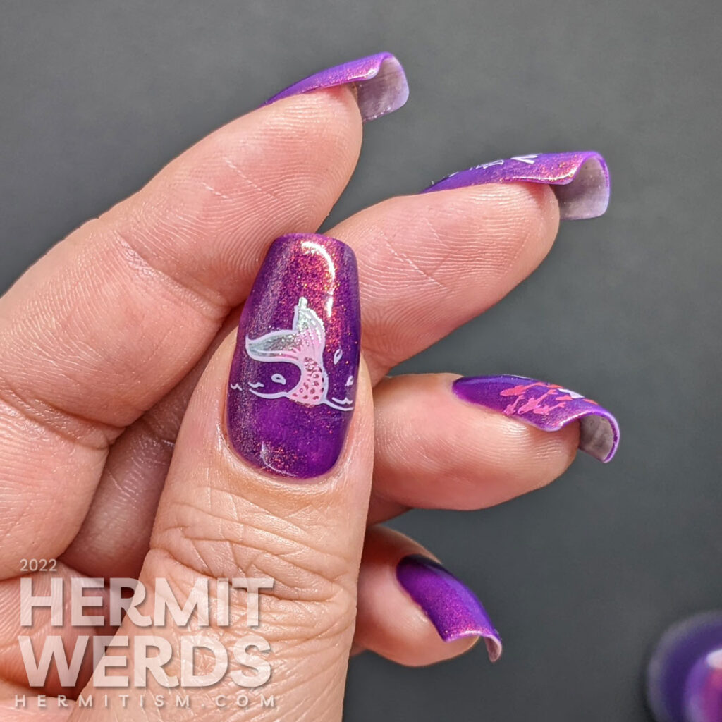 A purple shimmery mermaid nail art that says "In a sea of fish, be a mermaid" with mermaid, mermaid tail, and fish stamping images.