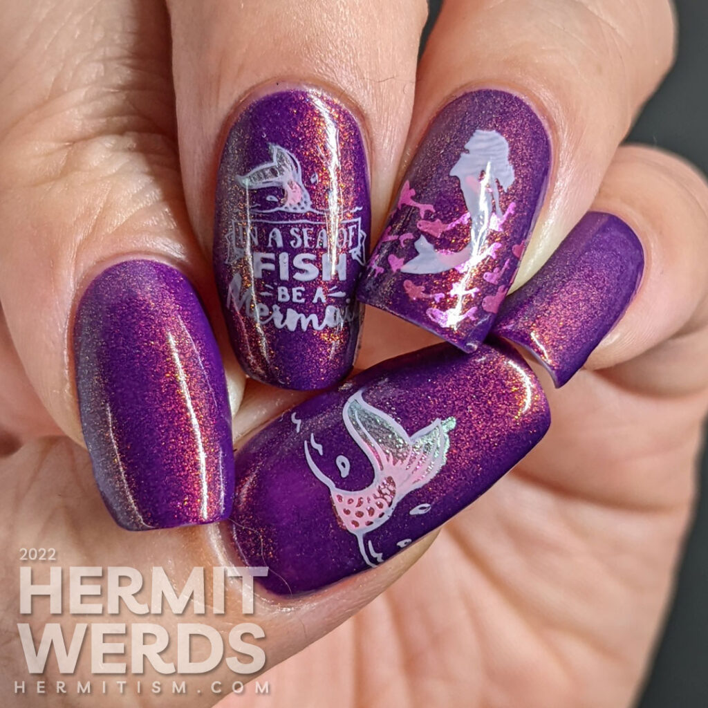 A purple shimmery mermaid nail art that says "In a sea of fish, be a mermaid" with mermaid, mermaid tail, and fish stamping images.