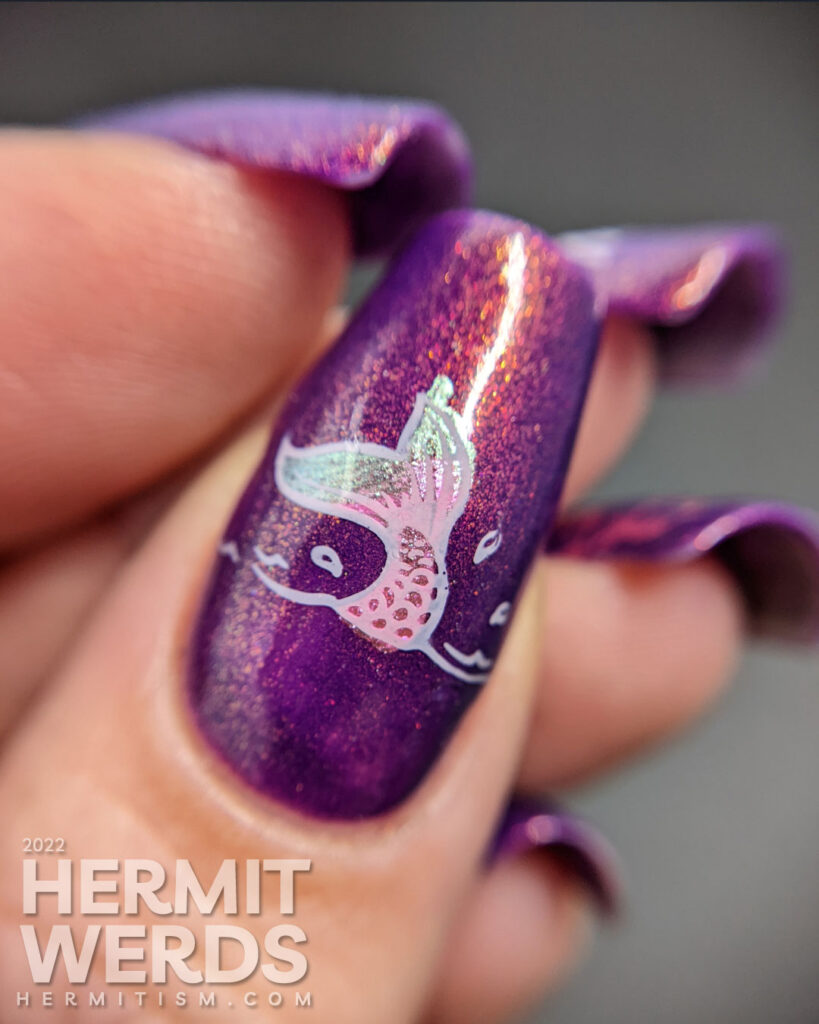 A purple shimmery mermaid nail art that says "In a sea of fish, be a mermaid" with mermaid, mermaid tail, and fish stamping images.