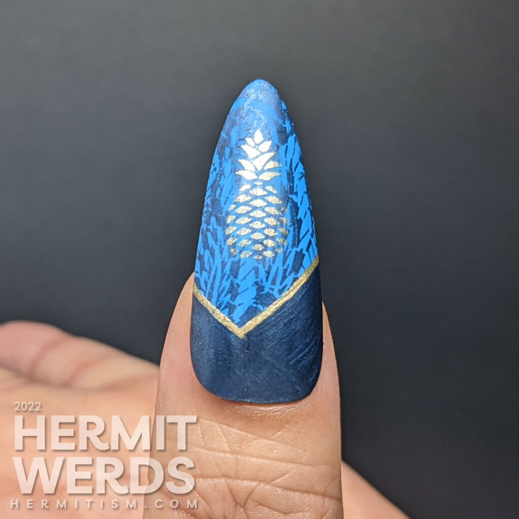 Golden pineapple nail art on blue stiletto falsies with a beautiful art deco lace pattern stamped in the background and half moons.