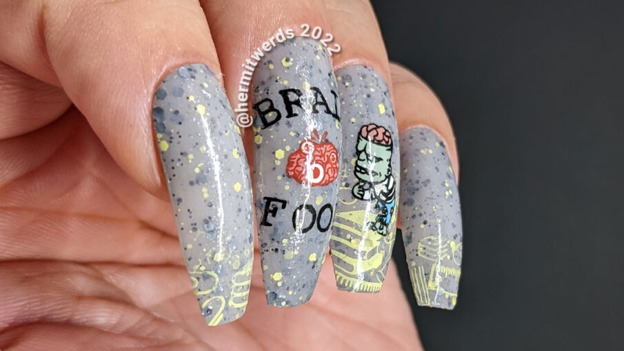 Zombie nail art on a grey crelly with stamping images of academic stuff, "Brain Food" w/brain, a zombie + a school being attacked by zombies.