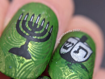 Happy Hanukkah nail art featuring menorah and dreidel stamping decals on a rich, green patterned background.