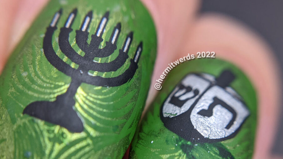 Happy Hanukkah nail art featuring menorah and dreidel stamping decals on a rich, green patterned background.