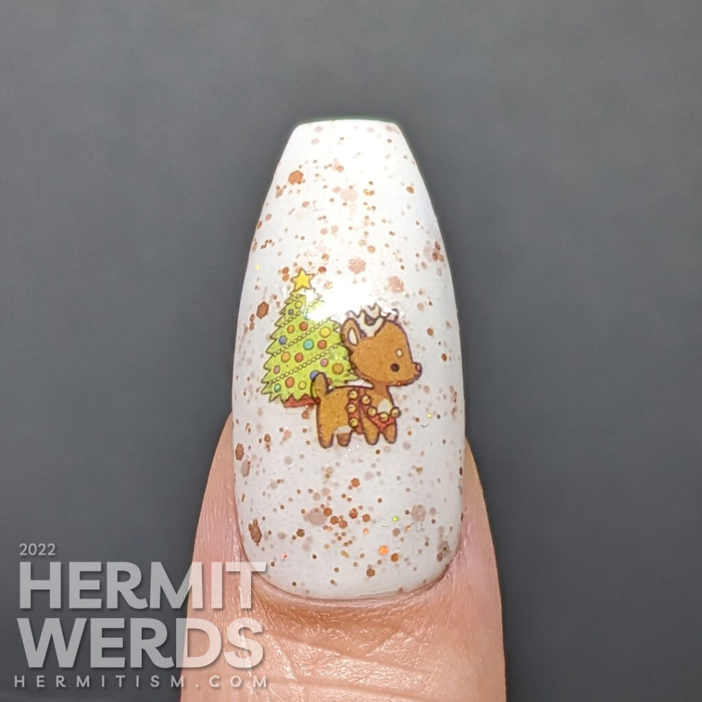 A gingerbread nail art with a Christmas tree and gingerbread people, house, and reindeer stickers on a crelly full of golden brown glitter.