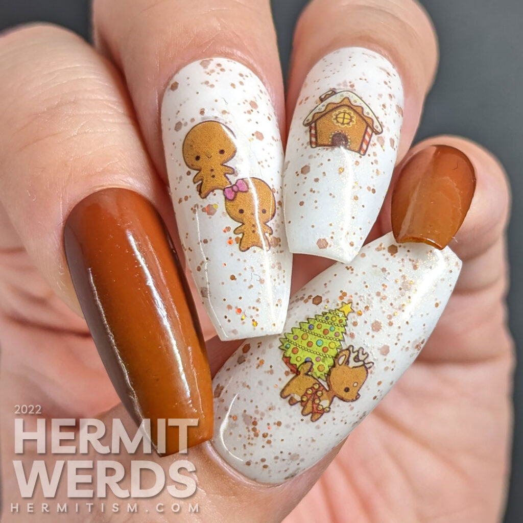 A gingerbread nail art with a Christmas tree and gingerbread people, house, and reindeer stickers on a crelly full of golden brown glitter.
