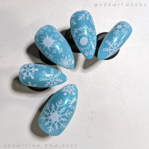 A cool blue nail art with white snowflakes stamped on a set of claw false nails.