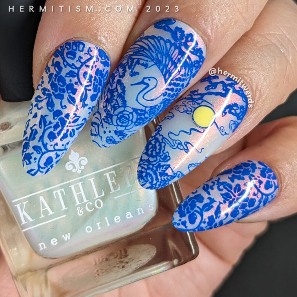 A Blue Moon nail art using a cobalt blue stamping polish with porcelain patterns over a white jelly nail polish with pink shimmer.