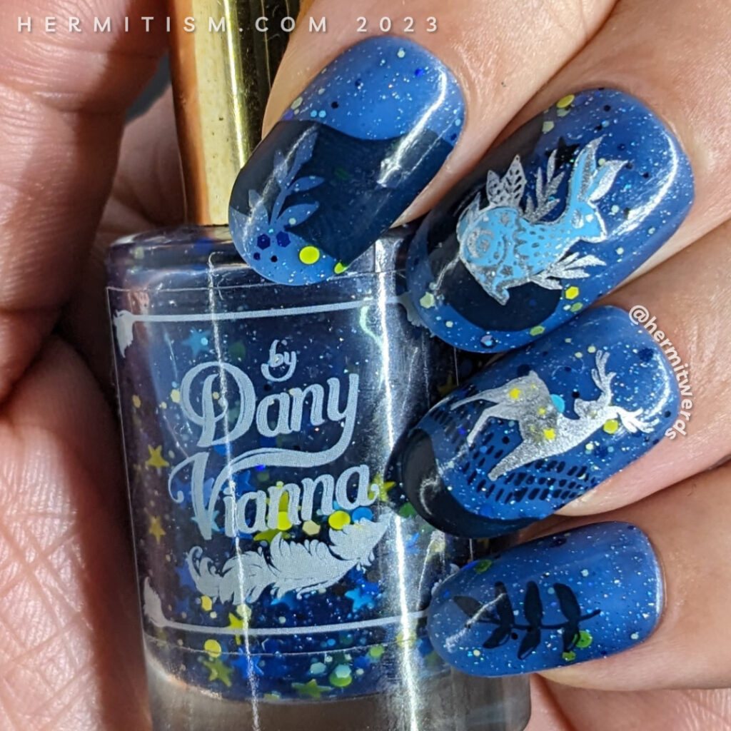 A celestial animal nail design with decals of a silver-outlined celestial deer, rabbit, and owl on a blue jelly sky with starry glitter.