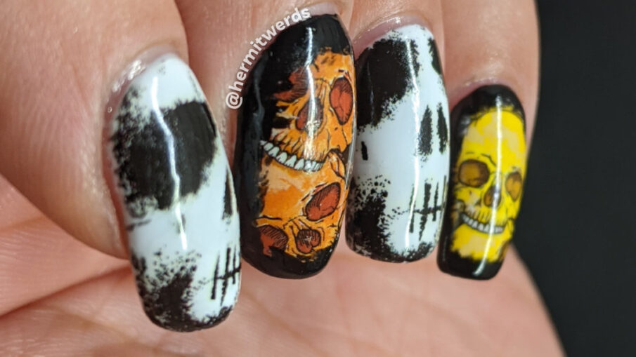 Skull nail art with skull water decals in white, black, orange, yellow, and green on a white background with black sponged around the edges.