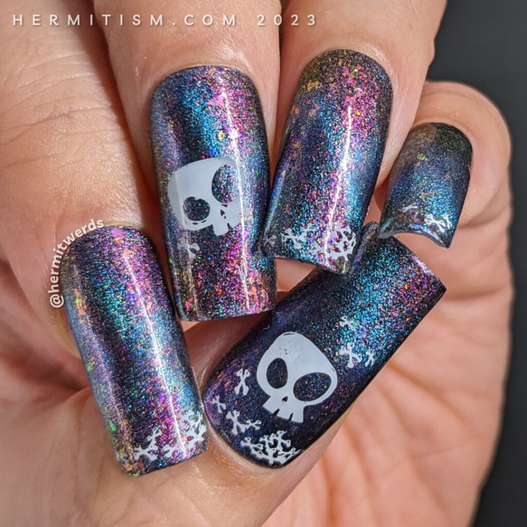 Simple skull and crossbones nail art on a purple/pink magnetic multichrome background filled with flakies and blue magnetic pull.