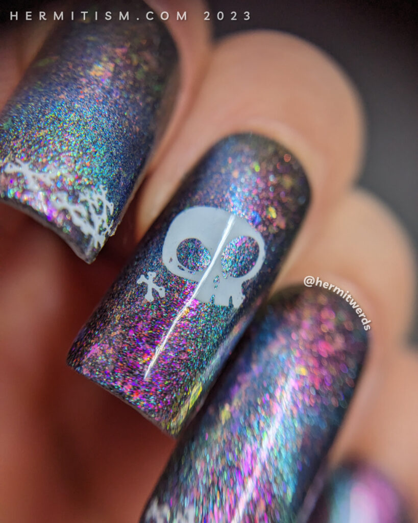 Simple skull and crossbones nail art on a purple/pink magnetic multichrome background filled with flakies and blue magnetic pull.