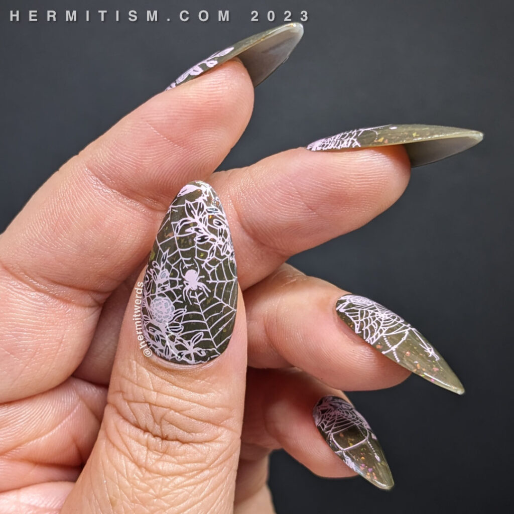Spider nail art of delicate, bejeweled spider webs with spider friends, framed by florals stamped on a dark musty green flakie polish.