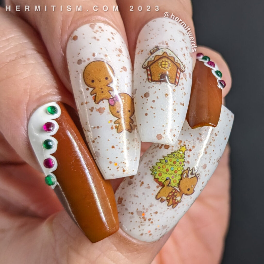 A gingerbread nail art with a Christmas tree and gingerbread people, house, and reindeer stickers and frosted edges with rhinestone gumdrops.