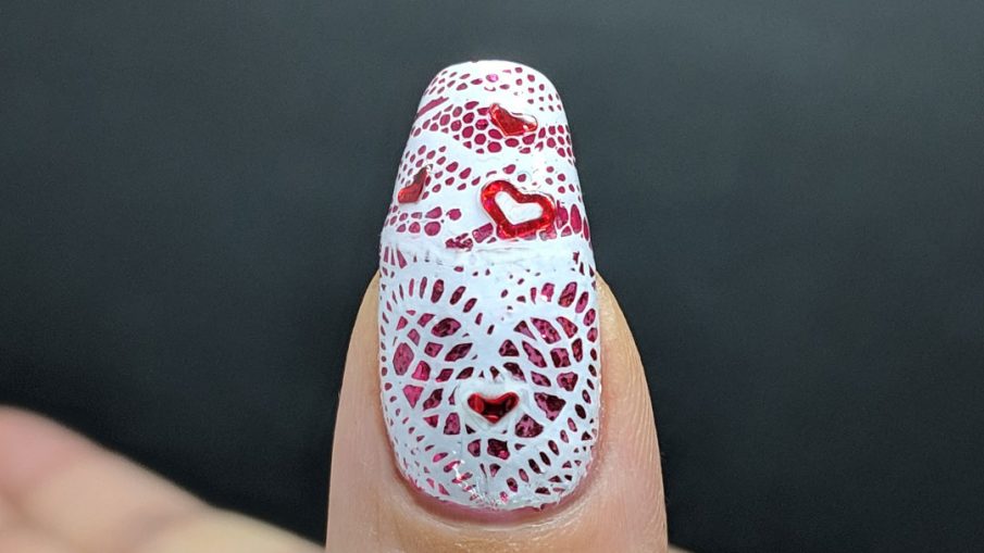 Lacy Heart - Hermit Werds - lace stamping in a heart shape over a glittery pink background with red heart sequins on top