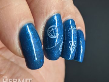 A medium blue polish with glitters and micro flakies with geometrically stylized cotton candy stamped on top.