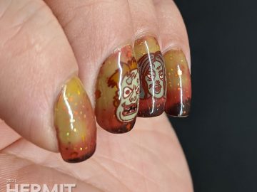 Zombie nail art with cartoon zombie head stamping decals and on a mustard/orange/brown tri-thermal base with orange and gold glitters.