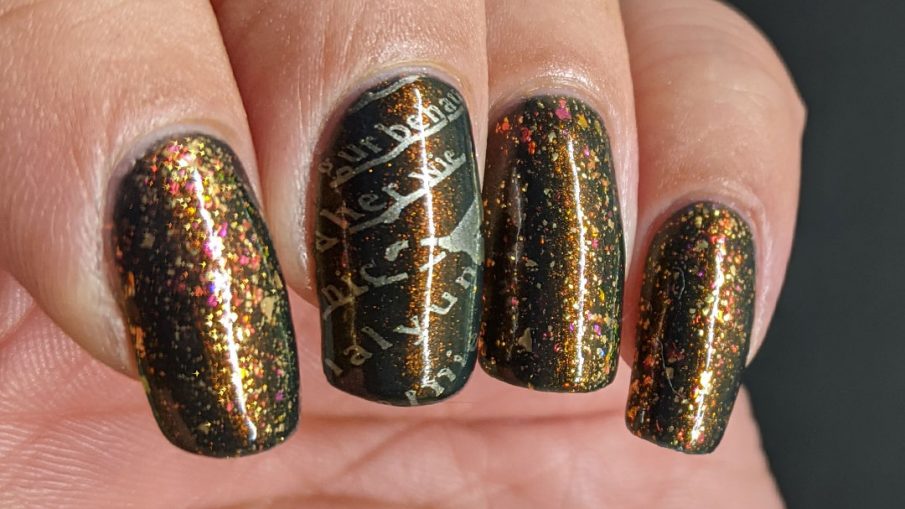 A smoky navy blue multichrome nail art with fake writing being highlighted (alphabet) stamping decals topped with a gold/iridescent topper.