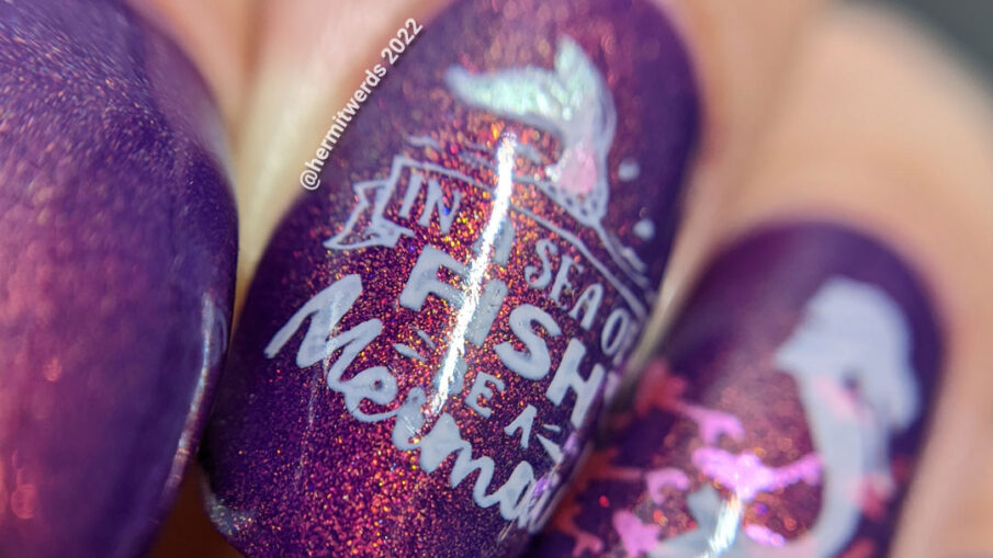 A purple shimmery mermaid nail art that says "In a sea of fish, be a mermaid" with mermaid, mermaid tail, and fish stamping images.