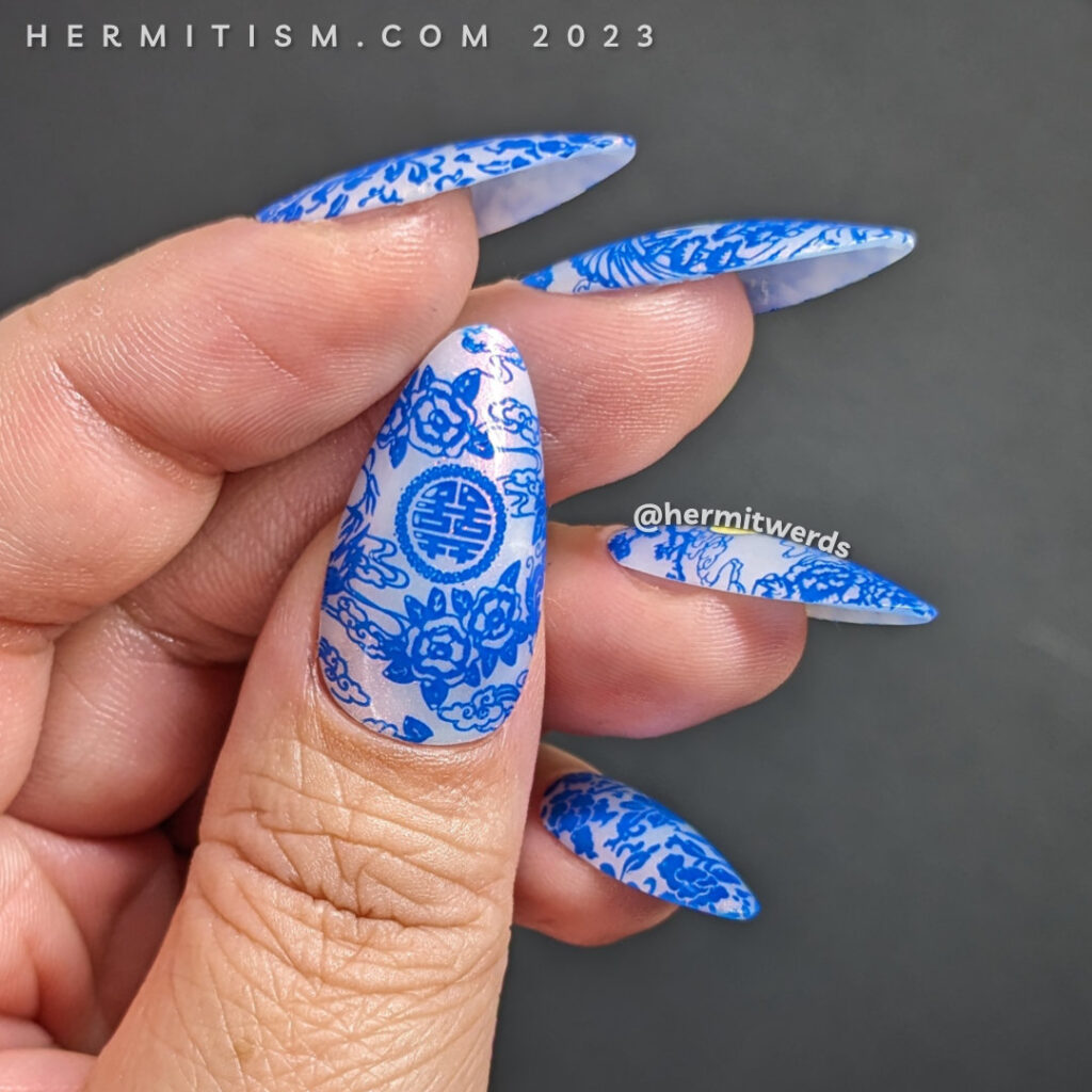A Blue Moon nail art using a cobalt blue stamping polish with porcelain patterns over a white jelly nail polish with pink shimmer.