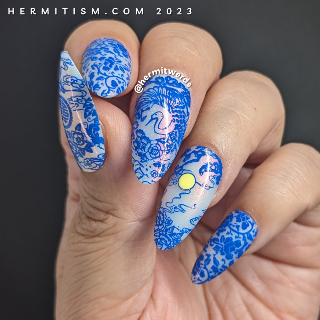 A Blue Moon nail art using a cobalt blue stamping polish with porcelain patterns over a white jelly nail polish with pink shimmer.
